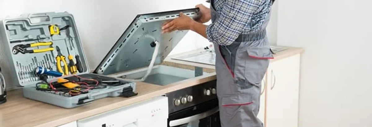 Cooktop repair technician lifting a built-in stovetop for service in Overland Park, KS