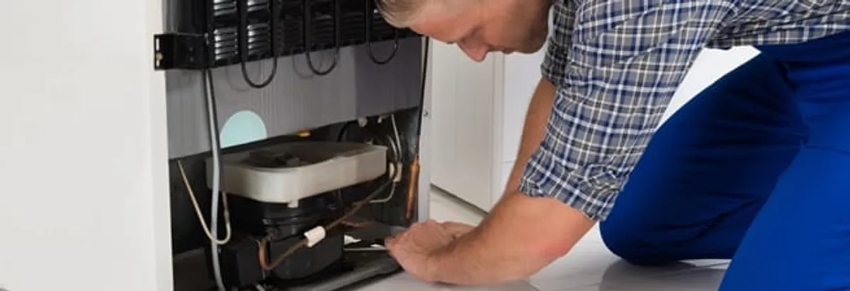 Refrigerator repair technician servicing the compressor and condenser area in Overland Park, KS